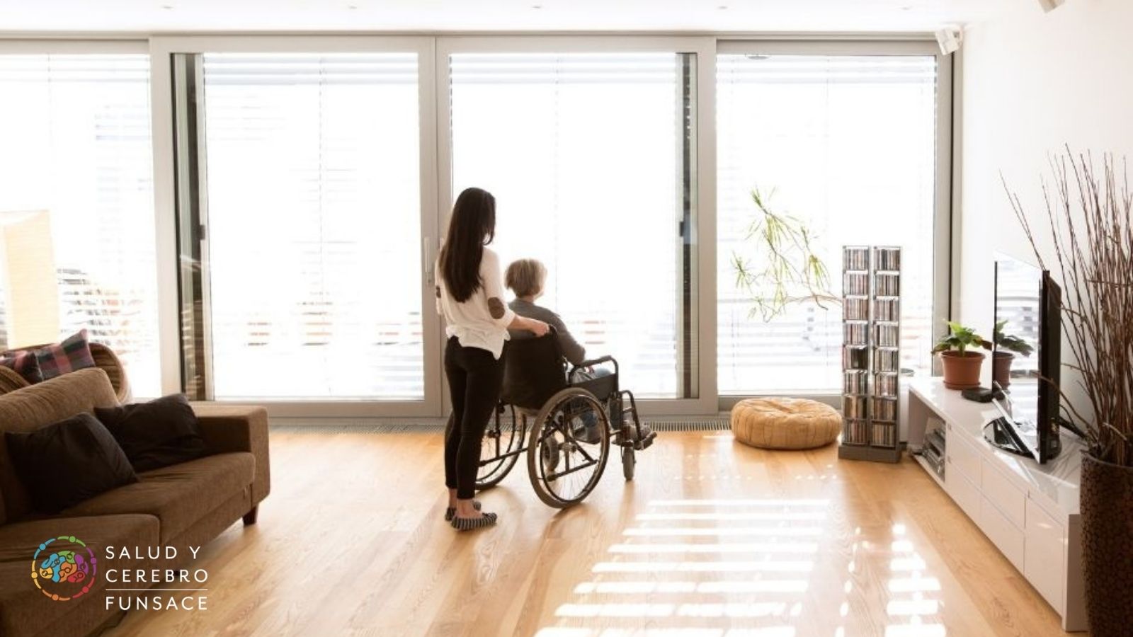 mujer joven llevando a mujer mayor en silla de ruedas dentro de una casa